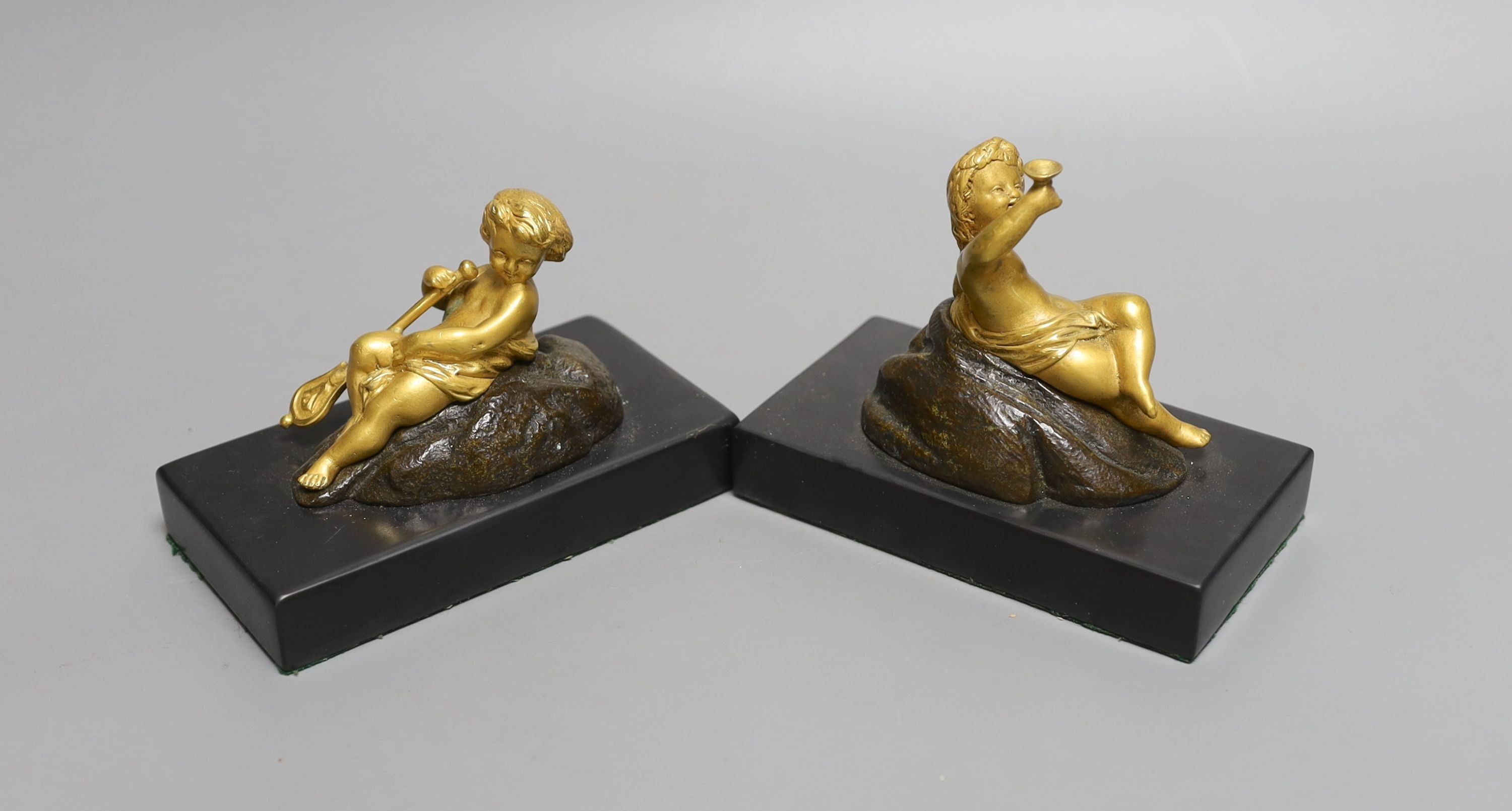 A pair of ormolu putto paperweights on black marble bases, 13 cms wide.